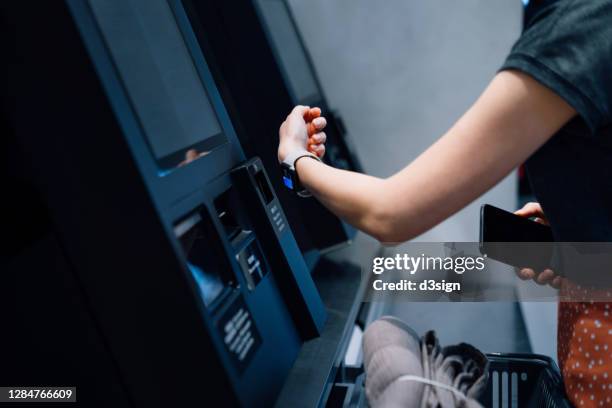 close up of a young asian woman using contactless payment via smart watch to pay for her shopping at self-checkout kiosk in a store - smartwatch pay stock-fotos und bilder