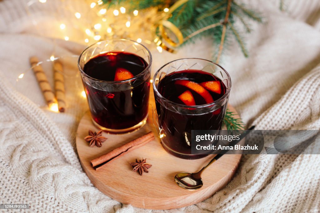 Two glasses with hot winter drink mulled red wine with orange slices, spices and knitted white Christmas background