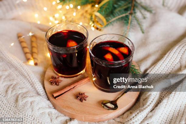 two glasses with hot winter drink mulled red wine with orange slices, spices and knitted white christmas background - christmas drinks stockfoto's en -beelden