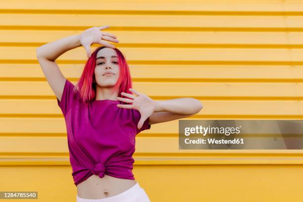 confident young woman with dyed hair dancing against yellow wall - purple shirt fotografías e imágenes de stock