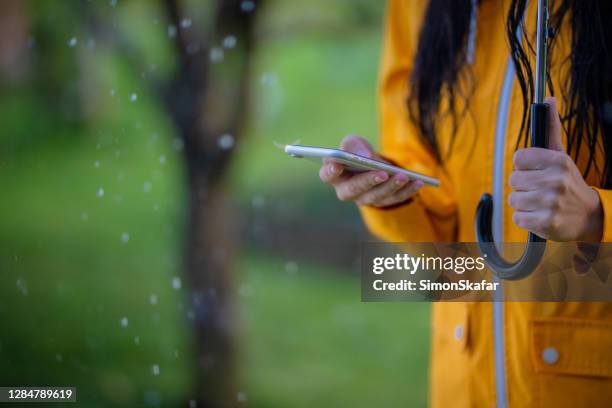 midsection of a woman in yellow raincoat using phone in the rain - rainy season stock pictures, royalty-free photos & images