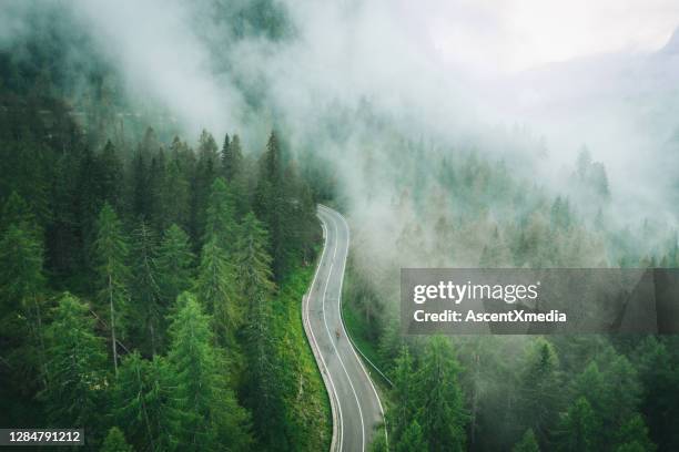 aerial perspective of road bicyclist riding up a wet road - green road imagens e fotografias de stock