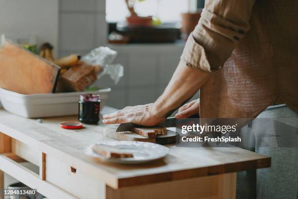 anonieme jonge mens die brood in de keuken snijdt - een close up - anonymous reporting stockfoto's en -beelden