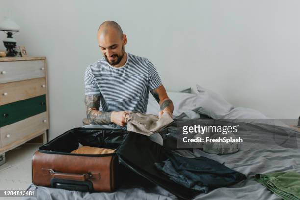 happy man sitting in the bedroom en verpakking zijn koffer voor een reis, travel concept (copy space) - holiday packing stockfoto's en -beelden