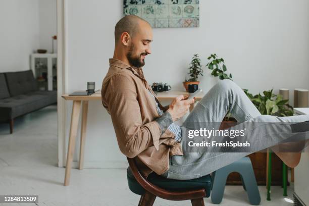 glimlachende jonge mens die aan zijn vrienden op sociale media spreekt terwijl terloops zitting in zijn flat - joggingbroek stockfoto's en -beelden