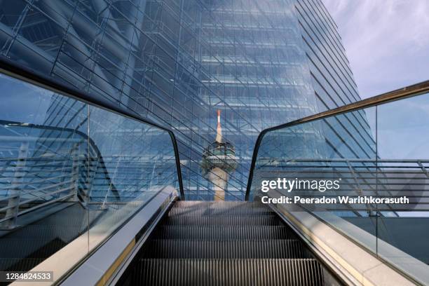 exterior, low angle and one point perspective view from escalator with background of reflecting rheinturm, rhine tower, on glass building's facade of stadttor tower. - building low angle stockfoto's en -beelden