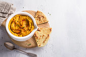 Delicious healthy homemade bean hummus with baked pumpkin, tahina and spices with flat bread on a light blue background