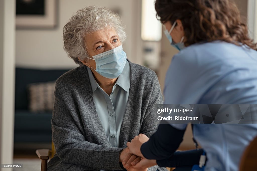 Female doctor consoling senior woman wearing face mask during home visit