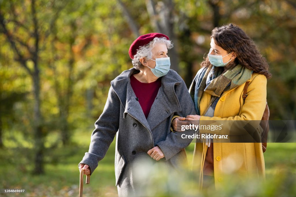 Senior woman with lovely girl wearing face mask at park