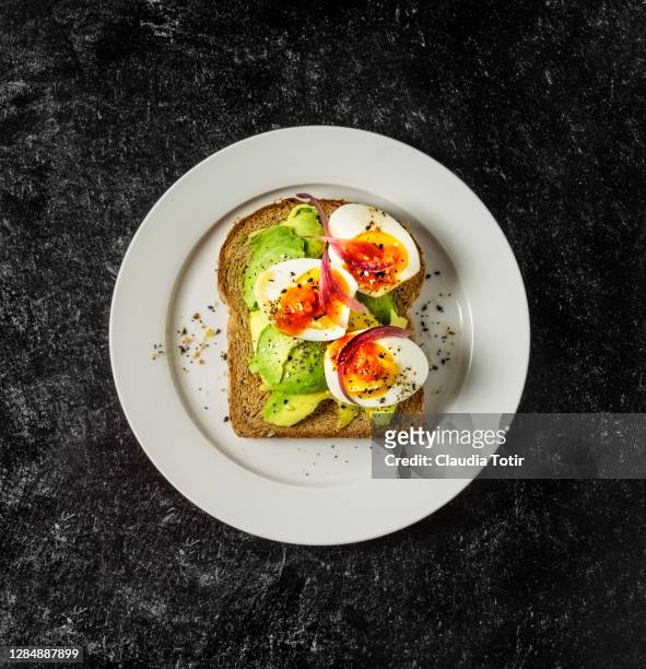 toast with boiled eggs and avocado on a plate on black background - hard boiled eggs stock-fotos und bilder