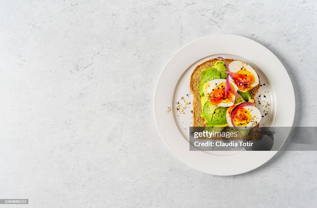Toast with boiled eggs and avocado on a plate on white background