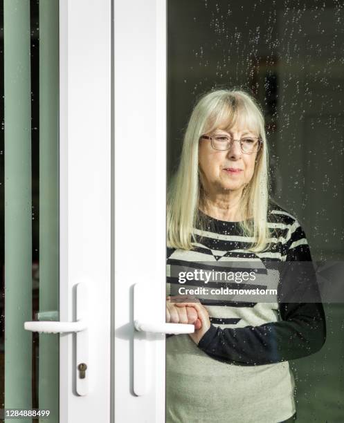 depressive seniorin schaut aus regennassem fenster - krankheitsverhinderung stock-fotos und bilder