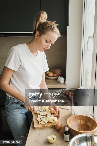 A woman in a white t-shirt and blue jeans prepares a festive Apple pie in the kitchen in front of the window A woman in a white t-shirt and blue jeans prepares a festive Apple pie in the kitchen in front of the window