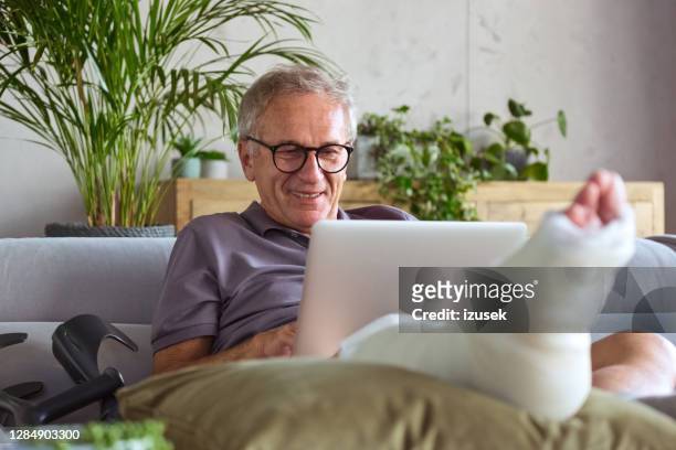 cheerful senior man with broken leg at home - broken leg stock pictures, royalty-free photos & images
