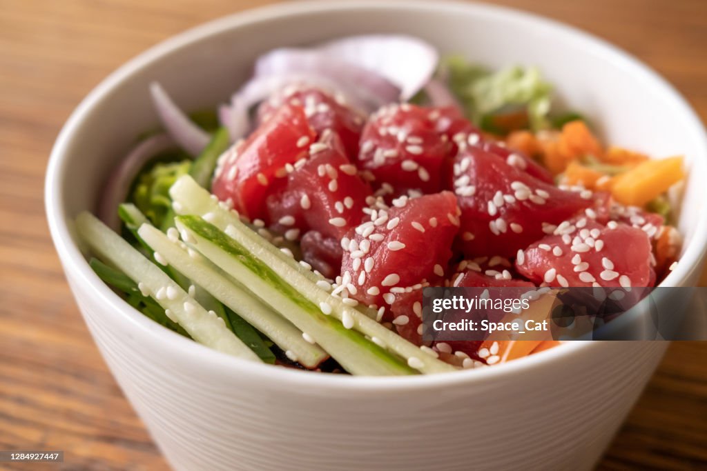 Healthy organic raw tuna poke bowl with cucumber, rice, carrots, onion served in bowl on wooden table. Healthy lifestyle