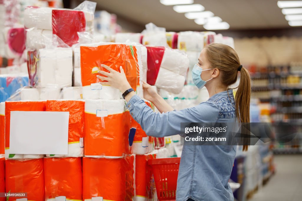 Young woman in protective face mask taking large pack of toilet paper
