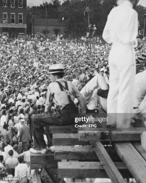Figure sits on wood-built structure looking across the crowd of approximately 20,000 people who had gathered to witness the public hanging of Rainey...