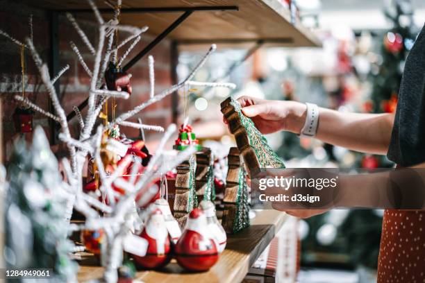 close up of young asian woman shopping for christmas ornaments on a retail display, looking at a sparkling christmas tree in a store - christmas decorations in store foto e immagini stock