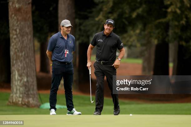 Phil Mickelson of the United States putts as Sir Nick Faldo of England looks on during a practice round prior to the Masters at Augusta National Golf...