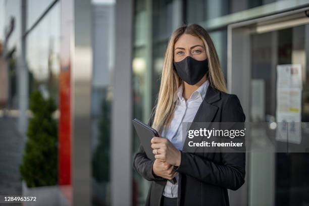 young well dressed sales woman wearing face mask and standing in front of car dealership with tablet - car dealership covid stock pictures, royalty-free photos & images