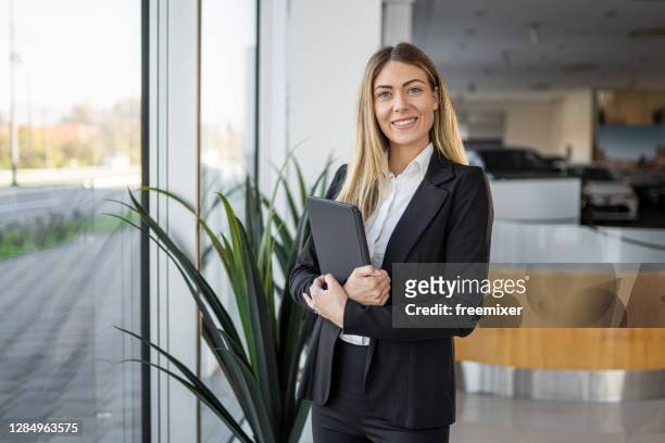 giovane ben vestita donna di vendita in piedi in concessionaria salone con tablet - venditore di automobili foto e immagini stock