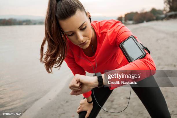 jeune coureuse de femme dans le sportswear emploie un traqueur intelligent sur la plage - fitness armband photos et images de collection