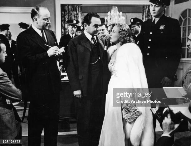 Edward G Robinson looking at Wendy Barrie with a room full of police present in a scene from the film 'I Am The Law', 1938.