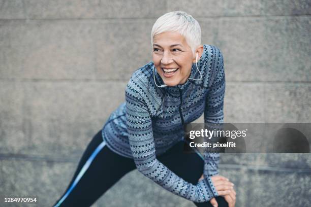 mature woman in sports clothing stretching outside - athleticism stock pictures, royalty-free photos & images