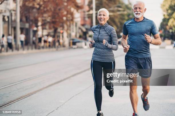 anziano uomo e donna anziano jogging fianco a fianco sulla strada - active seniors foto e immagini stock