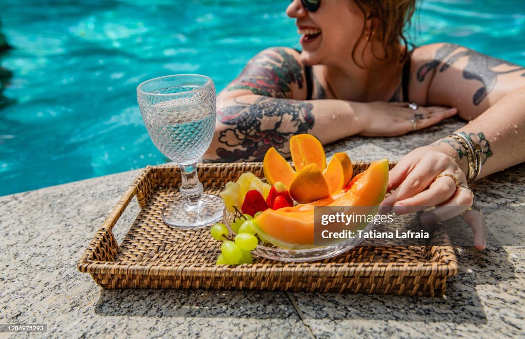 Woman eating fruits smiling the pool in a sunny day in the summer time