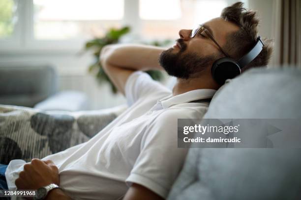 young smiling man with bluetooth headphones relaxing on sofa - teen meditating stock pictures, royalty-free photos & images