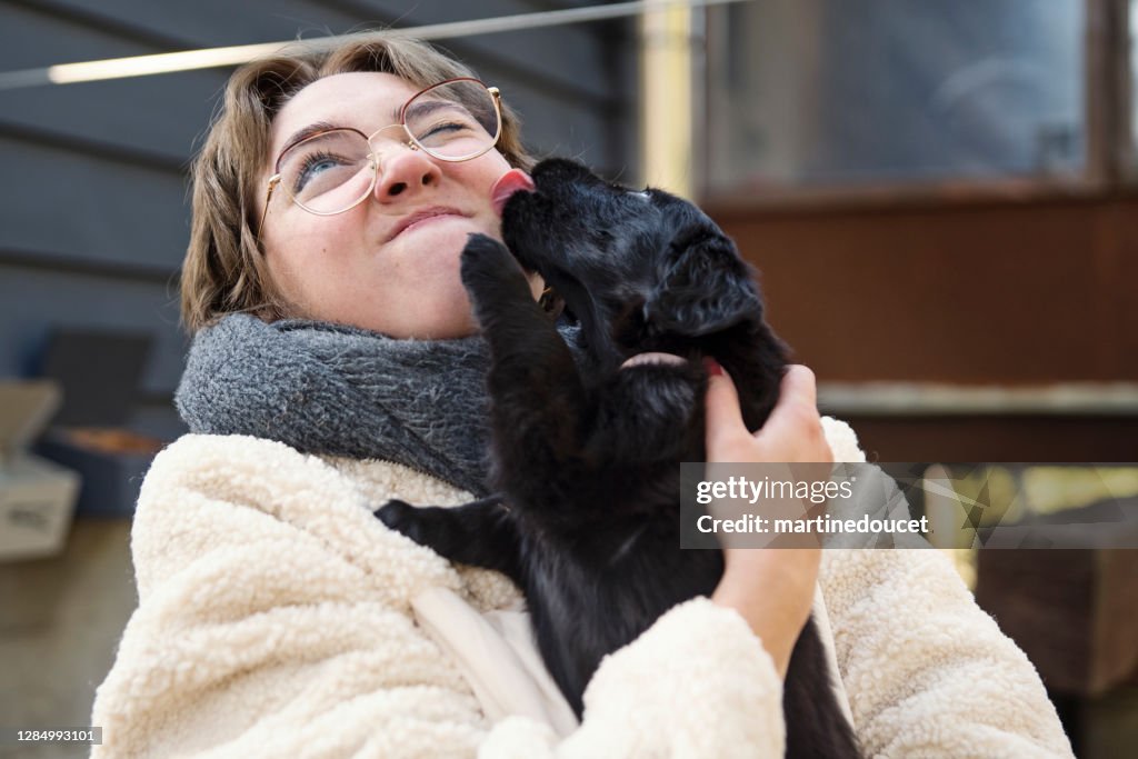 Young woman holding purebred flat-coated retriever puppy.