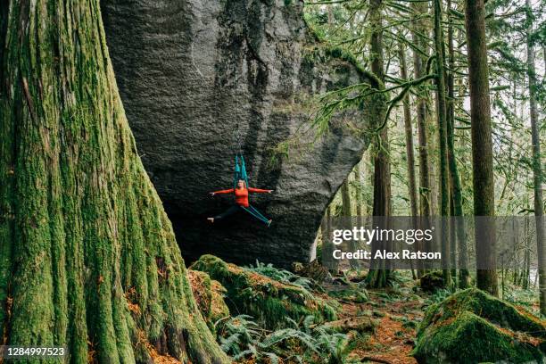 a young female adult performs acrobatic moves on an aerial hammock that is setup on a giant rock face - jungle gym stockfoto's en -beelden
