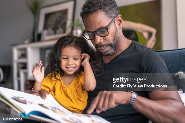 afectuoso padre leyendo libro con adorable hija de raza mixta - reading fotografías e imágenes de stock
