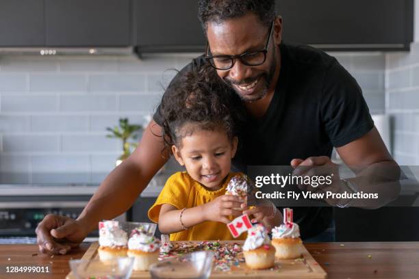 father and daughter decorate cupcakes while celebrating canada day at home - canada day stock pictures, royalty-free photos & images