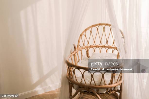 stylish scandinavian newborn baby nursery with natural rattan cradle and sheer white canopy hanging over it. - wieg stockfoto's en -beelden