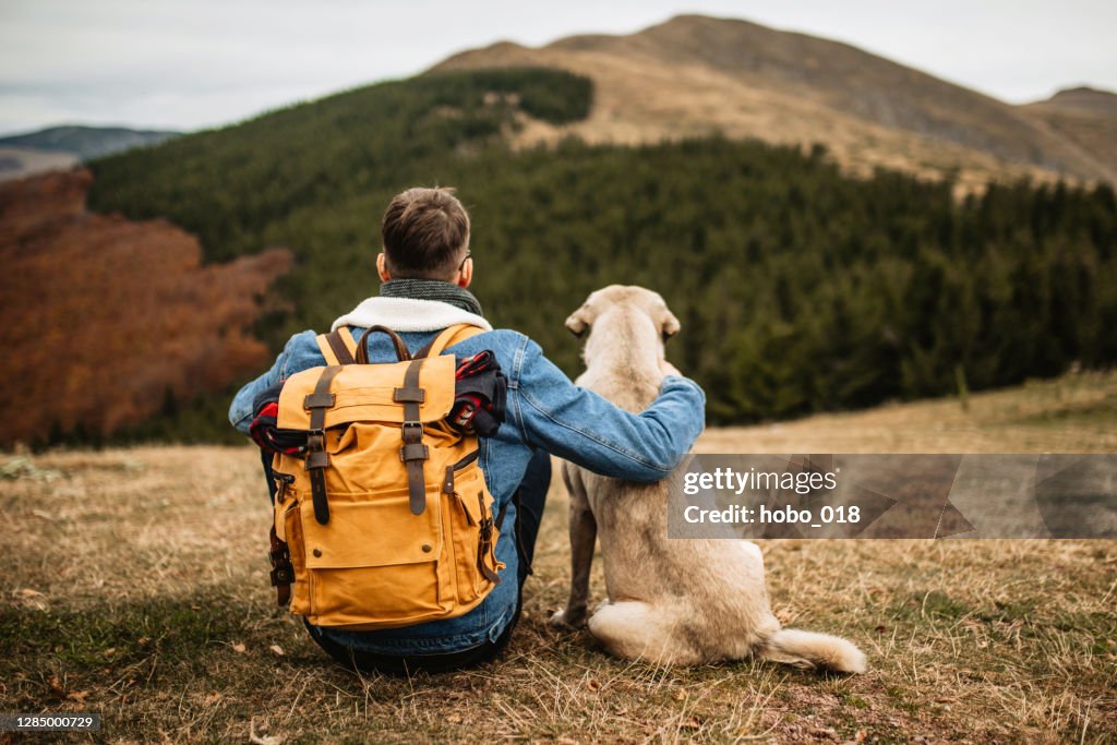 Hiker with backpack and his dog resting on mountain