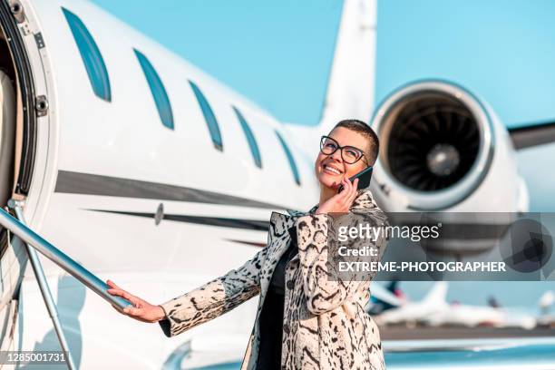 fröhliche geschäftsfrau telefoniert, während sie ins privatflugzeug steigt - first class plane stock-fotos und bilder