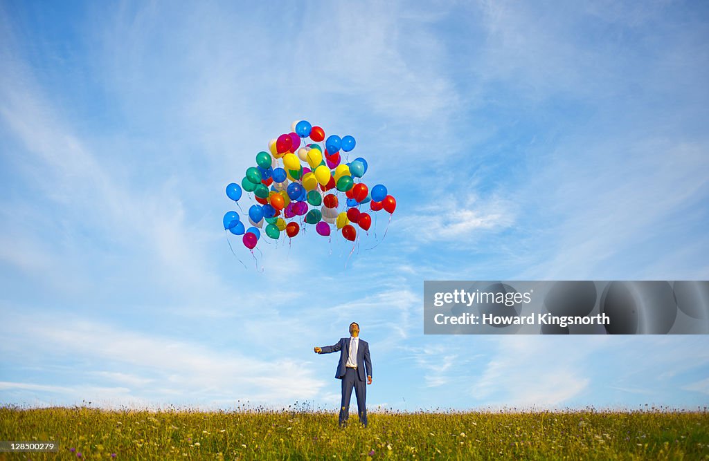 Businessman releasing big bunch of balloons