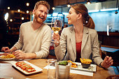 Smiling cheerful couple sitting in a restaurant, having dinner and chatting. Man talking to a woman while a woman listening to him and drinking white wine.