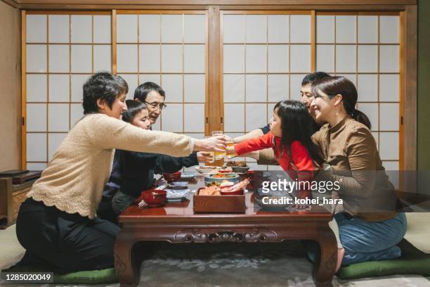 日本三代家庭在吃日本新年菜肴 osechi ryori 之前， 在日本房間的餐桌上喝著吐司 - 御節料理 個照片及圖片檔