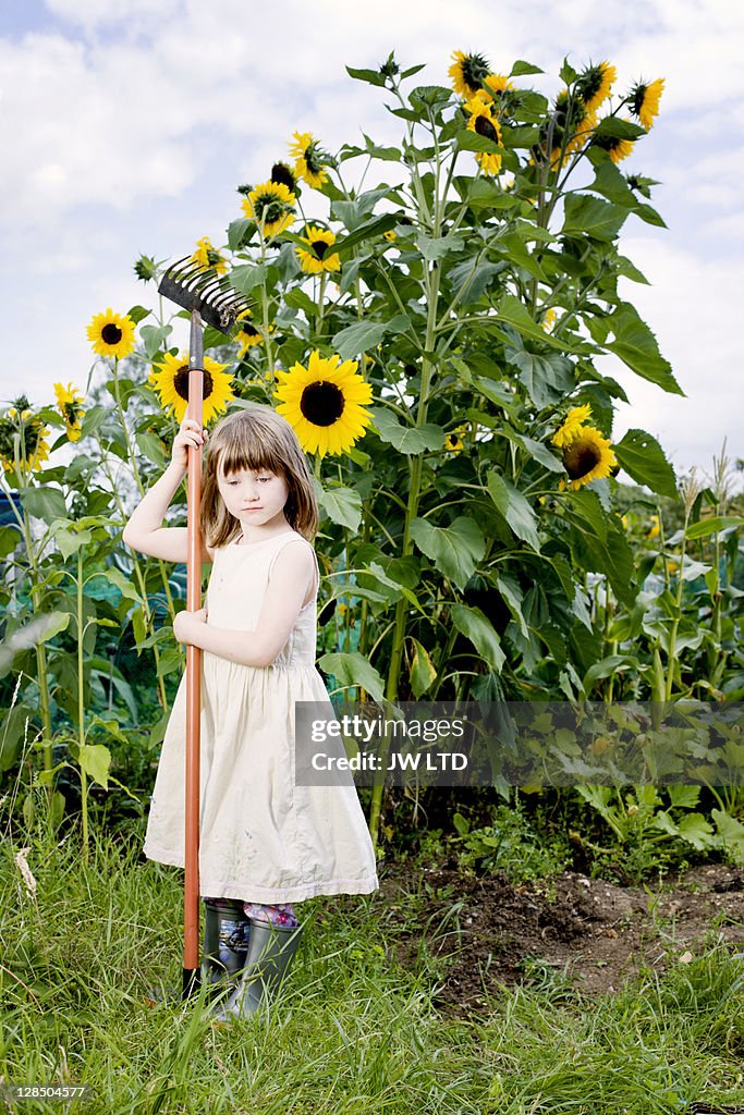 Girl with rake by sunflowers, portrait