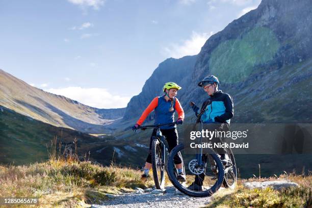 two mountain bikers on a bike trail stopping to check their smart phone - cycling scotland stock pictures, royalty-free photos & images