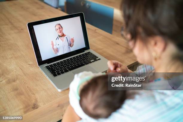 während des pandemieprozesses konsultiert die junge mutter, die mit ihrem laptop von zu hause aus einen videoanruf mit ihrem arzt führt, ihren arzt über den gesundheitszustand ihres neugeborenen. - baby monitor stock-fotos und bilder