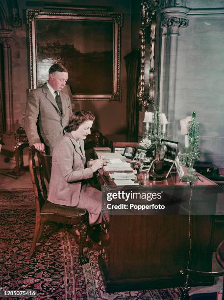 Bernard Fitzalan-Howard, 16th Duke of Norfolk posed with his wife Lavinia Fitzalan-Howard, Duchess of Norfolk seated at a desk in Arundel Castle,...