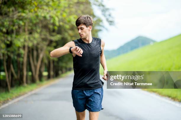 portrait of a caucasian male athlete using wearable run tracking technology while jogging on the street. healthy, active lifestyle concept. - polshorloge stockfoto's en -beelden