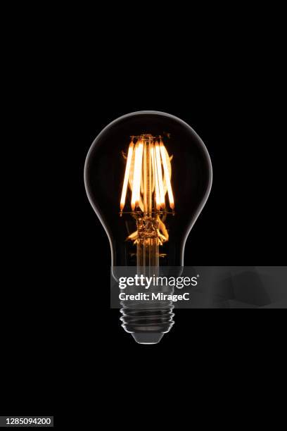 illuminated retro style light bulb on black - gloeidraad stockfoto's en -beelden