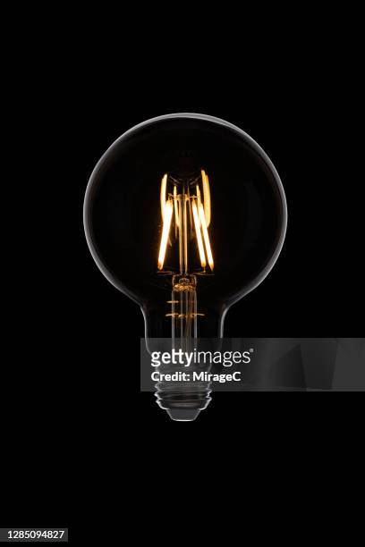 illuminated retro style light bulb on black - filamento fotografías e imágenes de stock