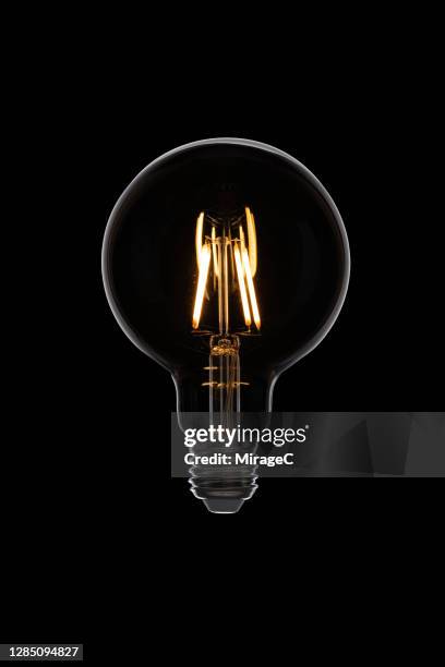 illuminated retro style light bulb on black - gloeidraad stockfoto's en -beelden