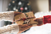 Woman in sweater giving a wrapped Christmas gift box to child. Glowing snow bokeh, fir tree. Winter holidays